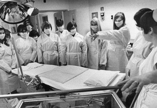 Students wearing face masks and sterile gowns visit the delivery room at Doctors Hospital as part of a family living class. The student on the right who is pointing is from Nicolet High School.