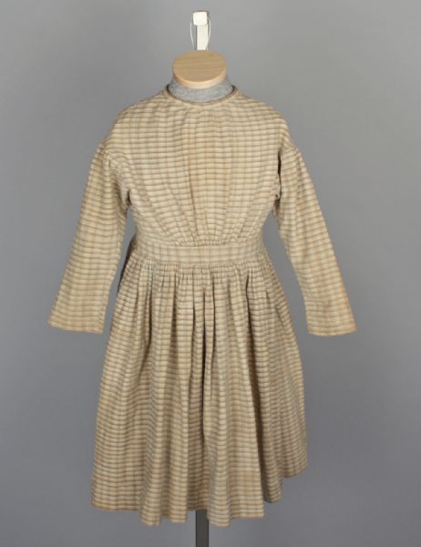 View of a long-sleeve, brown and white checked dress worn by Cora Cundiff.