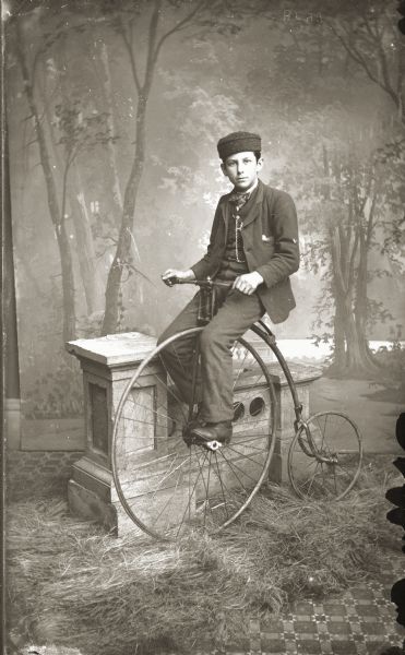 A studio portrait in front of a painted backdrop of young Ashley Bennett posing on a bicycle.