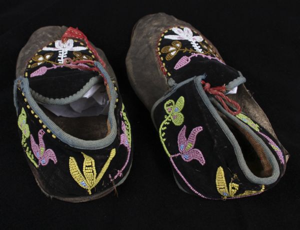 View from the heel of a pair of dark brown leather moccasins beaded in yellow, pink, green and white floral and plant designs. The moccasins were created around the Great Lakes. A type of moccasin typical of the Menominee and Potawatomi, circa 1900.