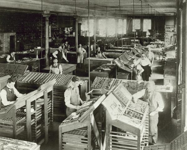 Elevated view of male printers, hand-setting type in the workroom at J.H. Yewdale Printing Company.