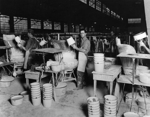 Several men dip pitchers and pails to apply metal at Vollrath Company.