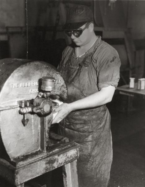 A man wearing safety goggles and an apron while working in a machine shop. He may be part of a safety program.