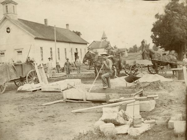 Construction workers on the job, with horse-drawn wagons in the background.