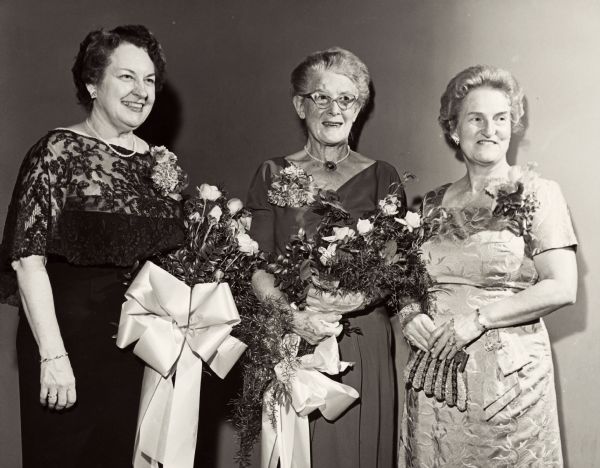 Three Civics Club members pose together; two of them are holding flower arrangements. From left to right are: Mrs. Conrad Elvehjem, unidentified woman, and Mrs. James Woodburn.