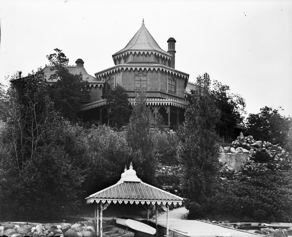 The rear view of the Ceylon Building, which was from the World's Columbian Exposition in Chicago. The building was later purchased by J.J. Mitchell, moved to Lake Geneva and converted to a private residence. A pier and two small boats under a decorative roof are in the foreground. 