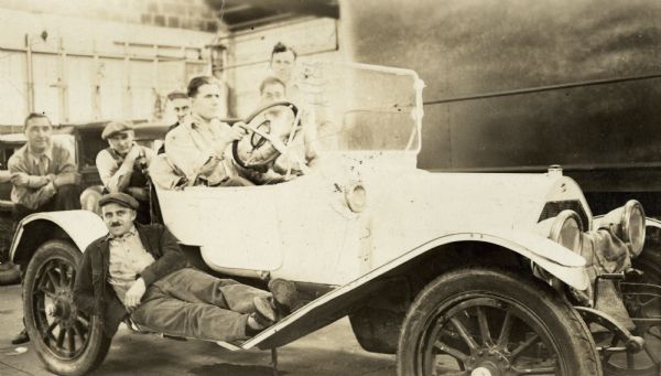 Employees of the Ideal Body Company sitting in and around a car.