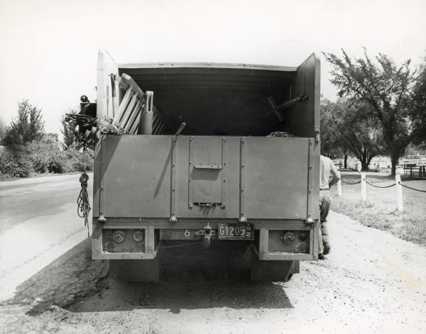Rear view of a bed box built by the Ideal Body Company for the Wisconsin Power and Light Company. A man is standing on the right of the truck, which is parked on the side of a road.