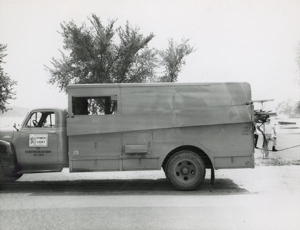 Wisconsin Power and Light truck with bed box built by the Ideal Body Company. Two men are standing by a fence behind the truck on the right near a lake.
