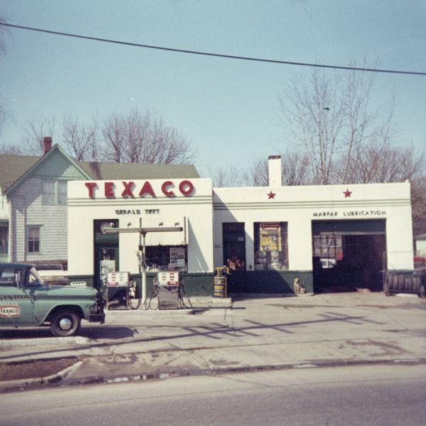 View from street of exterior of the Texaco Station located at 448 Park Street owned by Gerald Tifft. There is a dog sitting near the open garage door.