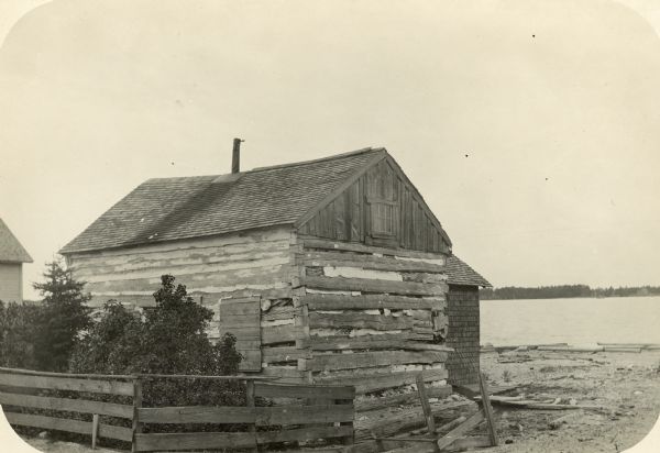 Ruins of a Mormon cabin built of squared logs. A harbor is visible in the background.