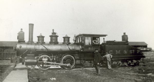 Left side view of Chicago,Milwaukee & St. Paul Railway locomotive engine no. 901, class J2, built by Borrks Locomotive Works in 1887. Engineer Jake Rhyner is leaning on the step, fireman Julius Wilman sits in the cab, and switchman Richard Allen stands in front with a pipe in his mouth.