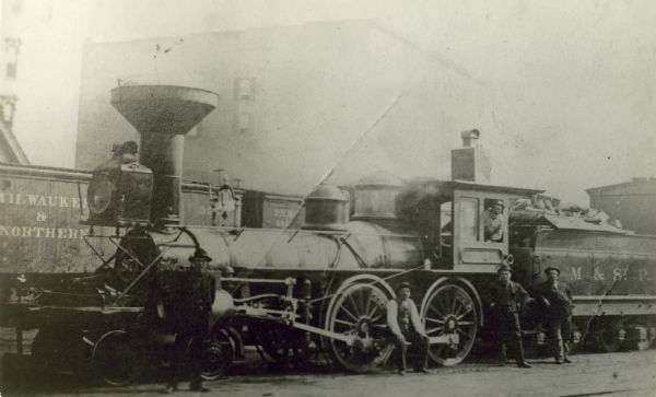 Several men pose with the Chicago, Milwaukee & St. Paul Railway engine #87, built by Schenectady Locomotive Works. This image was taken near Cherry Street.