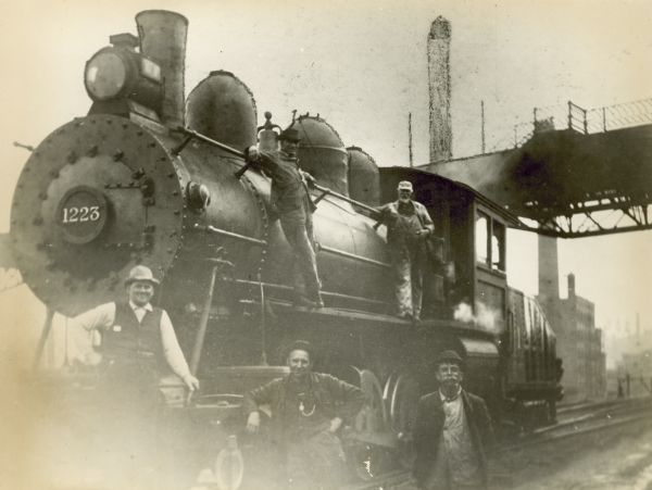 Five railroad employees pose on Chicago, Milwaukee & St. Paul Railway engine no. 1223 at the Chestnut Street yard. Left to right are yardman Jack Meyer, yardman Oscar Rosgosch, yardman Michael Market, fireman Harry F. Bell, and engineer Fred J. Schultz.