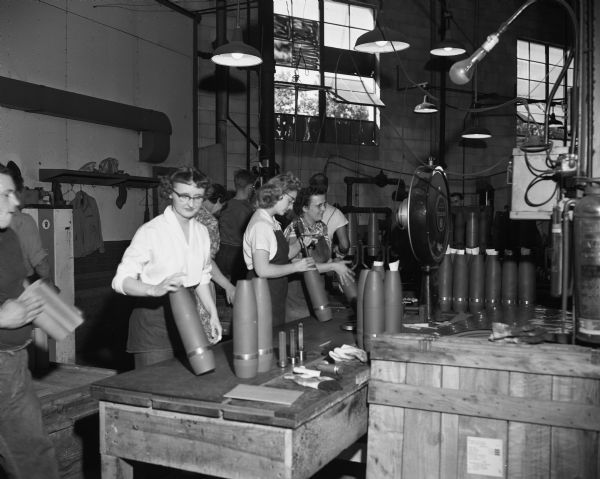 Men and women employed by Malleable Iron Range Co. making artillery shells to be used in the Korean War.