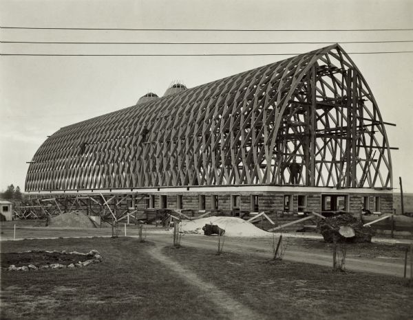 Exterior view of foundation and elaborate frame of a Gothic roofed barn, partially built.