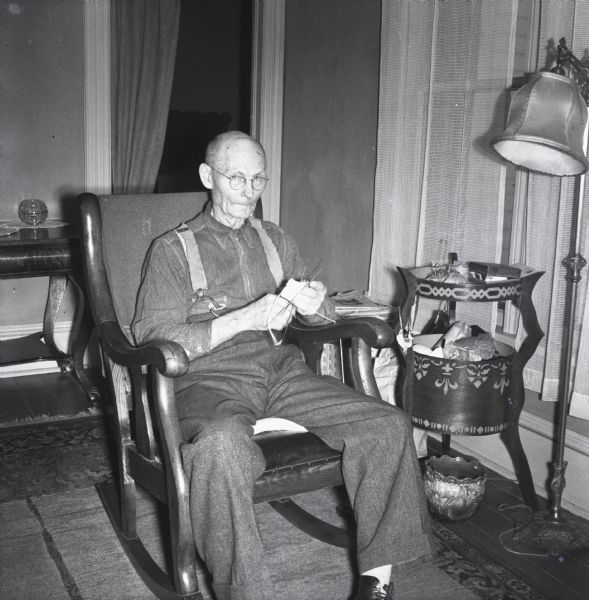 Elderly man sitting in a rocking chair and knitting.