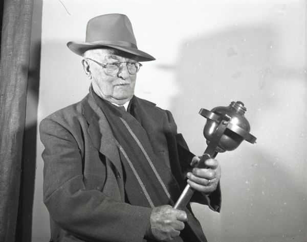 William Scott, former torch boy, holding one of the kerosene torches used in fire fighting in the 1880's.