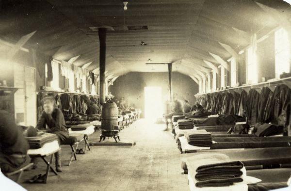Interior view of Civilian Conservation Corps barracks at Devil's Lake State Park. Several men can be seen sitting leisurely on their bunks. Two heating stoves are also visible.