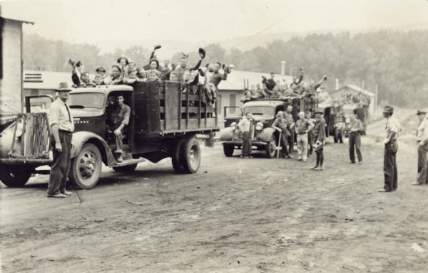 Civilian Conservation Corps workers at the Devil's Lake State park camp waving from trucks. Others men stand in the dirt road nearby.
