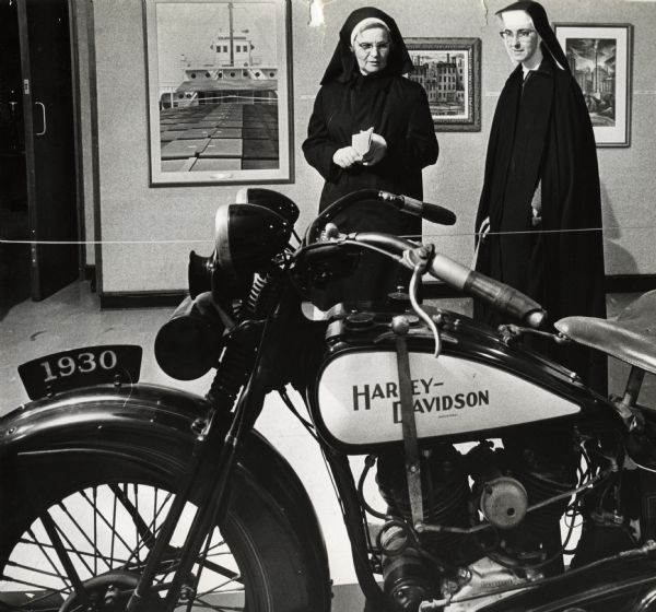 Teachers from St. Rose Catholic School, 514 N. 31st St., Sister Mathia (left) and Sister Geran, visited a show of the artworks of the 1930's in the mezzanine gallery of the Milwaukee Art Center. They are looking at a 1930 Harley-Davidson motorcycle. Three paintings can be seen on the wall behind the women.