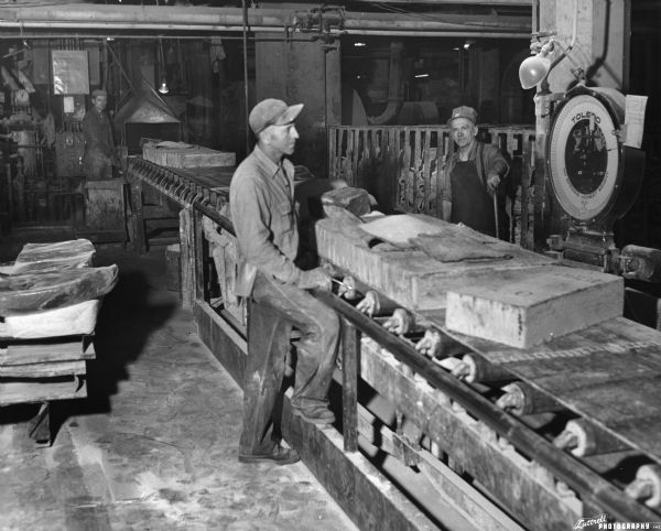 Two men work at a conveyor belt at a tire production plant.