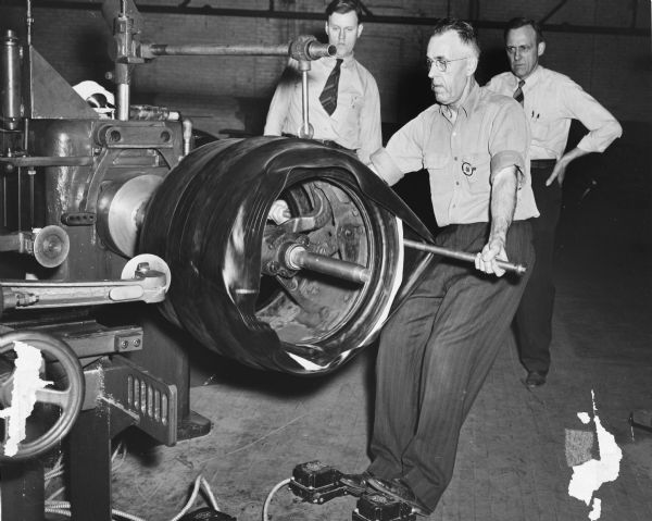 Bill Mcnair rolls the tread onto a tire as two other men look on at the Rubber Company's Gillette Tire Plant.