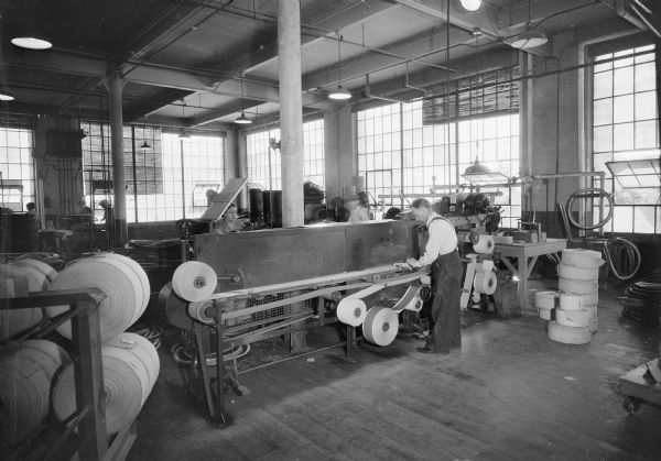 Workroom in the Uniroyal factory where men and women are building tires.