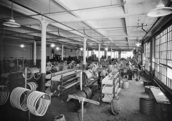 Elevated view of men working with long strips of rubber and fabric while making tires.