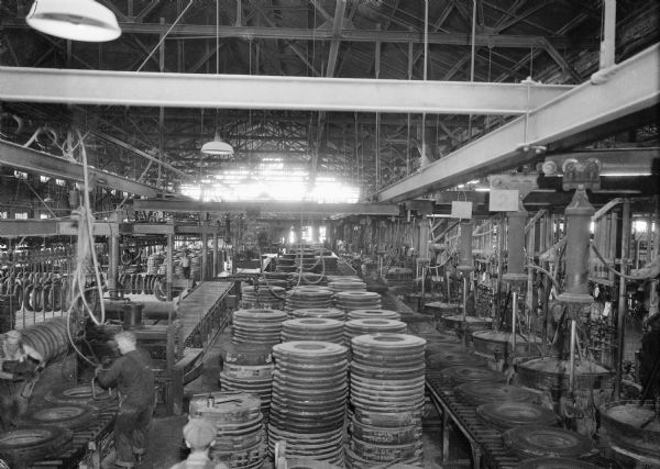 Elevated view of stacks of tires siting in the Uniroyal factory. Men work at machinery building tires.