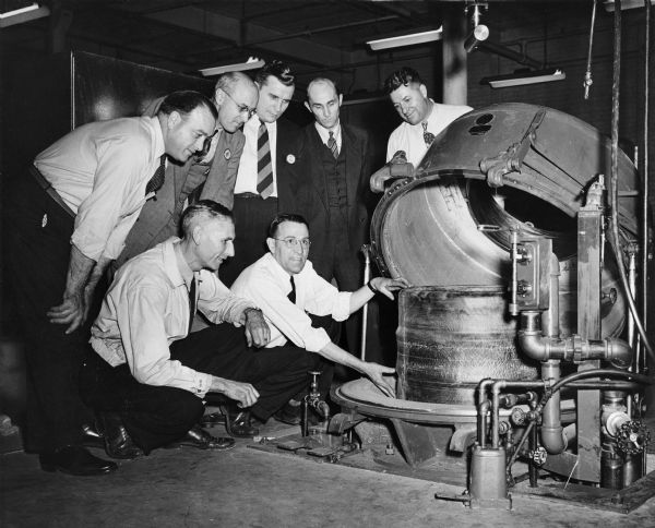Seven men pose together as the first raw tire at the Gillette Tire Plant is put into a vacuum expander.