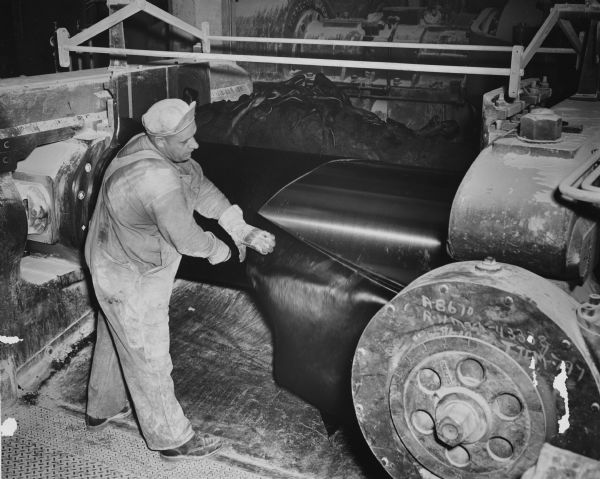 Elevated view of Tom Ellington cutting rubber from a roll to make a tire at the Gillette Tire Plant.