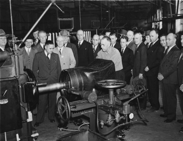 Tire builder William (Bill) McNair puts a pocket on the first tire built at the Gillette Tire Plant. Civic representatives and employees of construction firms and of the plant watch him. From left to right are H.O. Hutchens, E.K. Collison, R.Y. Copland, E.S. Potter, W.F. Campbell, E.B. Mertes, M. M. Kelly, N.B. Patten, J.F. Reheiser, H.T. Helfrich, C.E. Stare, Rex Hovey, C.R. Johnson, G.V. Rork, R.L. Scott, G.F. Baker, K.H. Stubenvoll, O.B. Eldred, G.H. Bennett, Jr., and R.L. Chatterson.