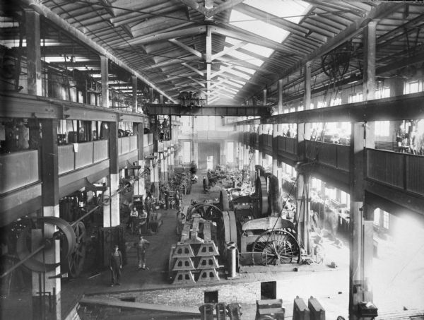 Interior elevated view of an Allis Chalmers factory. Men are posing on the factory floor.