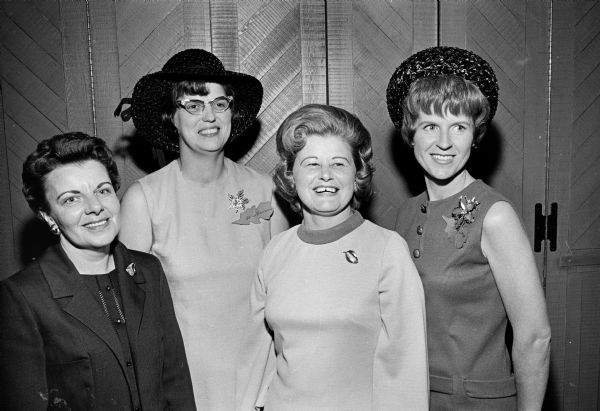 Four members of the Who's New Club pose together at the Who's New fall luncheon. Two of the women wear leaf-shaped name tags.