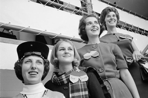 Four members of the Who's New Club pose together on a stairwell. Three of the women are wearing an acorn-shaped name tag.