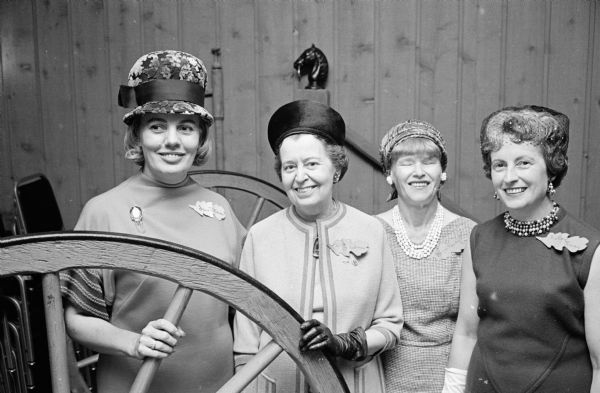 Four members of the Who's New Club pose between wagon wheels at the Who's New fall luncheon. Each woman wears a leaf-shaped name tag.