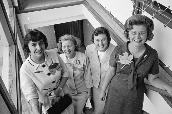 Four members of the Who's New Club pose on a stairway at the Who's New fall luncheon. Each woman is wearing a leaf- or acorn-shaped name tag.