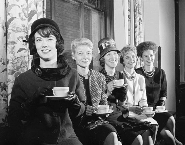 Five members of the Who's New Club pose sitting together holding teacups/coffee cups on saucers.