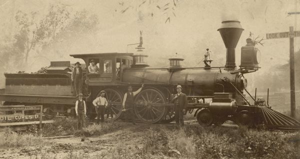 Side view of Chicago, Milwaukee & St. Paul Railway engine no. 294, which is decorated with antlers above the headlight, a miniature cannon mounted above the pilot or cow catcher, and archery figures mounted on top of the headlight and also the whistle. Billy Emerson was the engineer and his son Billy was the fireman.