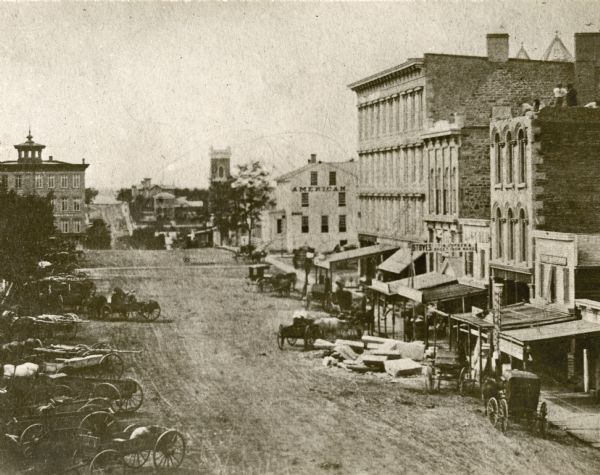 Daguerreotype of elevated view of Pinckney Street, looking northwest. View includes the American House and Bruen's Block, both on the corner of East Washington Avenue. Visible in the distance at the right end of Pinckney Street (on what is now called Mansion Hill) is the two-year-old Bashford House. The public streets are lined with busy stores and crowded with wagons, hacks and carriages, and merchants' refuse.