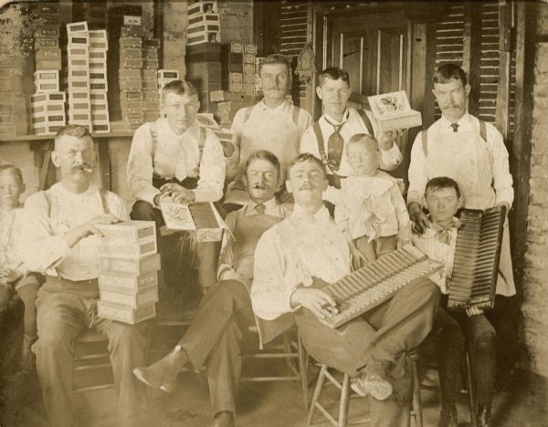 Workers at the Willms cigar factory, Milwaukee, Wisconsin, posing with cigars and cigar boxes. Gustav Willms (c. 1854-1917) sits on the far left with six cigar boxes on his knee. His son Edward Willms (b. 1886) sits on the far right with a cigar mold in his hands. The other workers are not identified. The cigar factory was in the back of the Willms house.