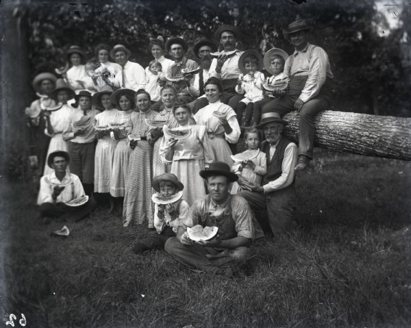 Outdoor group portrait of the Goetsch and Evans families all eating watermelon at a picnic.