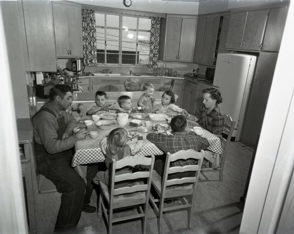 Mother, father, and seven children seated at a kitchen table eating dinner.