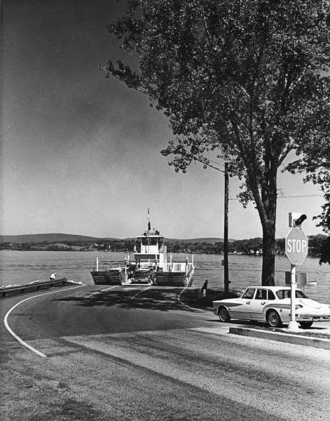 View from road of the ferry "Colsac II" arriving at the shoreline of the Wisconsin River, with an automobile on the right waiting to board.