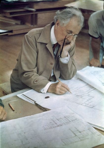 Architect Frank Lloyd Wright working at a drafting table.