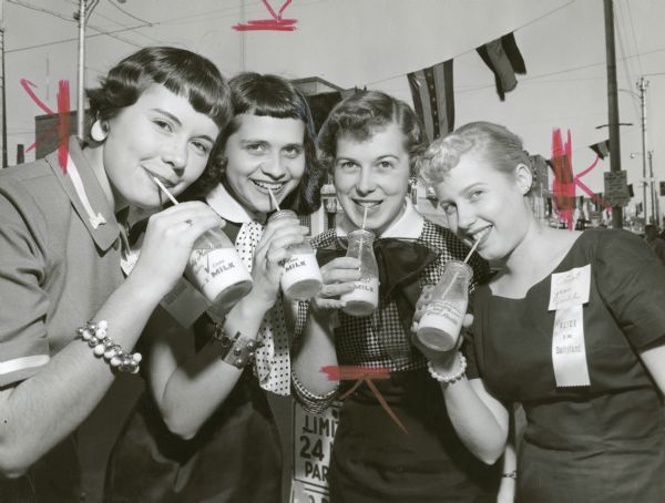 Four candidates for Alice in Dairyland pose together drinking bottles of milk with straws. From left to right are: Betsy Bachhuber of Mayville, Cheeril Hope Heublin of Beaver Dam, Doris Olsen of Brooklyn (Green and Dane counties), and Carol Jean Gould of Peshtigo.