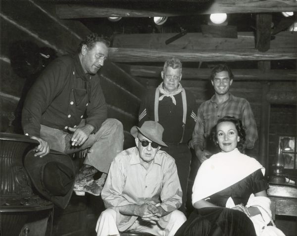 Director John Ford (in glasses and a hat) on the set of the film "The Searchers," with actors including John Wayne (left) and Doris del Rio. Behind them stand Jack Pennock and Jeff Hunter.