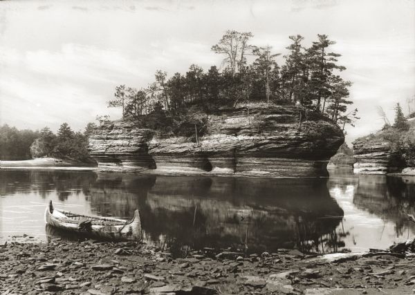 View of Lone Rock on the Wisconsin River. A canoe is floating along the shoreline in the foreground.