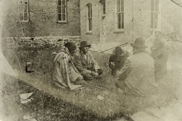 Group of five Ho-Chunk (Winnebago) men seated on the lawn outside a building waiting for their annuity payment.
